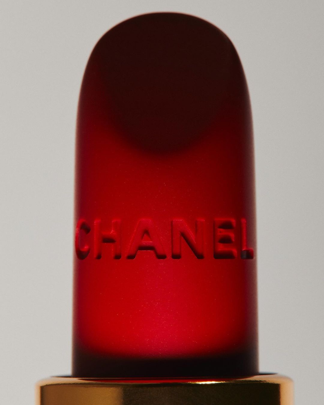 Close-up of a red Chanel lipstick with embossed branding against a neutral background, showcasing beauty and luxury.