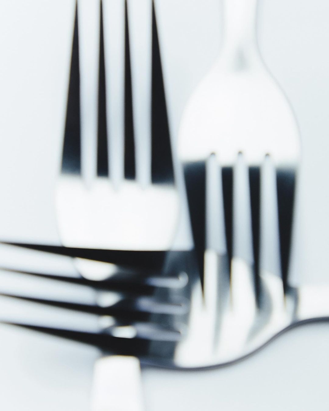 Close-up studio shot of two shiny metal forks stacked on top of each other against a bright white background, displaying simple elegance.