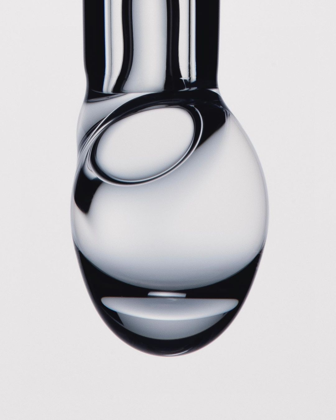 Close-up photograph of a clear, stylized glass carafe featuring minimalist design and reflective light play against a bright, neutral background.
