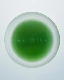 Top-down view of a round frosted glass jar with a vibrant green interior and embossed text on a pale background.