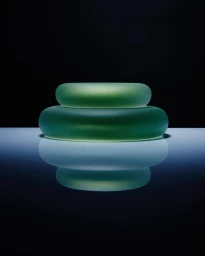 Two stacked translucent green glass objects resting on a reflective surface against a dark background