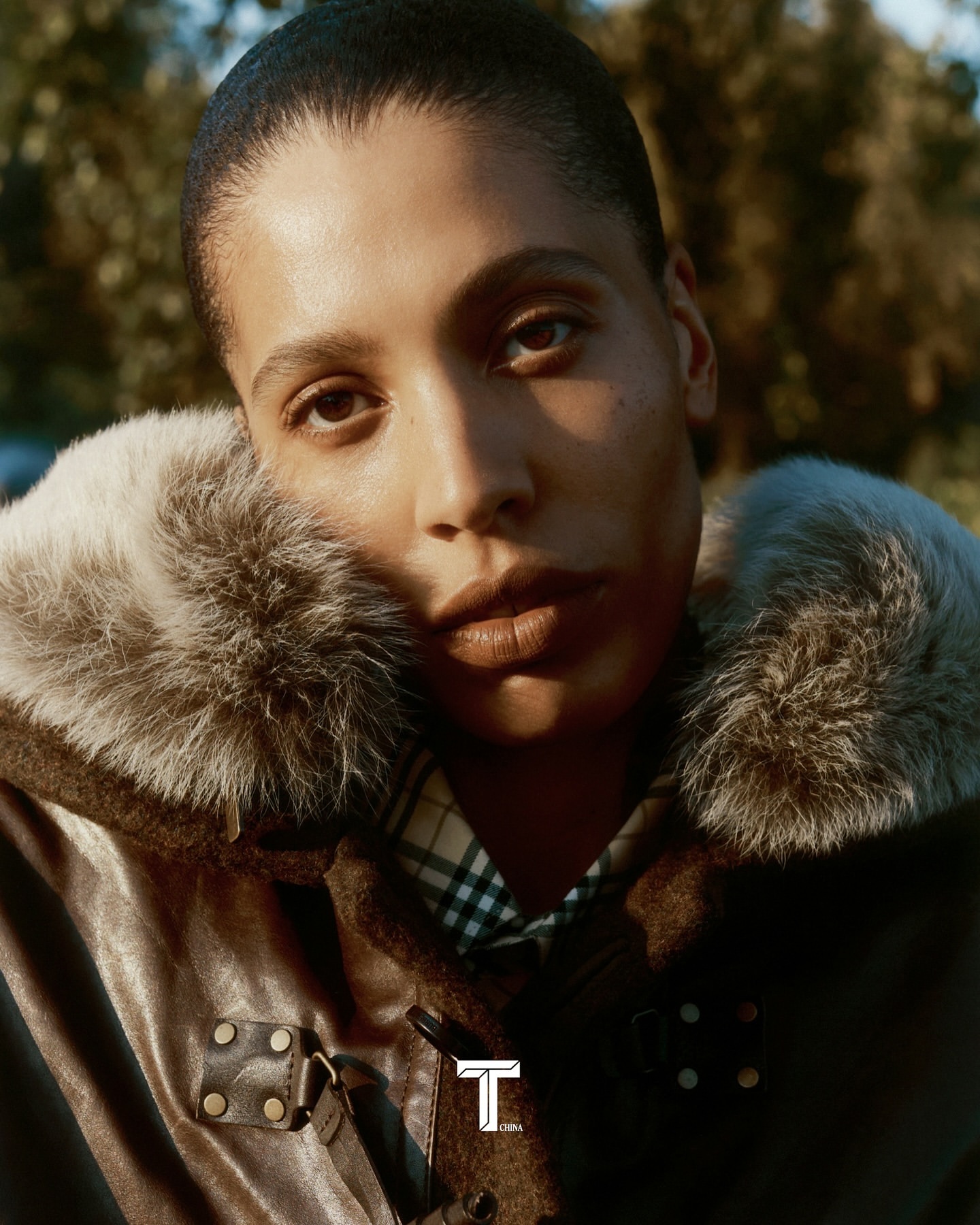 Portrait of a woman with short hair wearing a leather jacket with a fur collar, posing outdoors with natural lighting in the background.