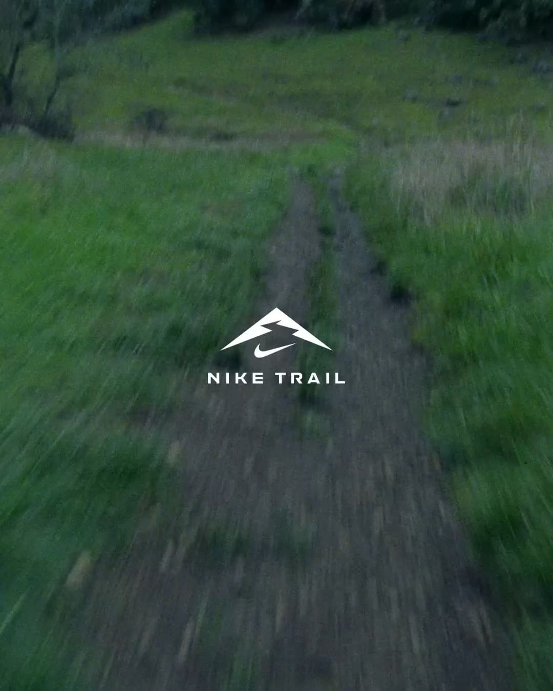 Nike Trail logo on a dirt path surrounded by green grass and trees, creating a natural environment for a running or hiking trail.