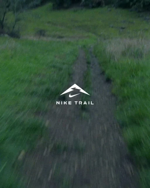 Nike Trail logo on a dirt path surrounded by green grass and trees, creating a natural environment for a running or hiking trail.