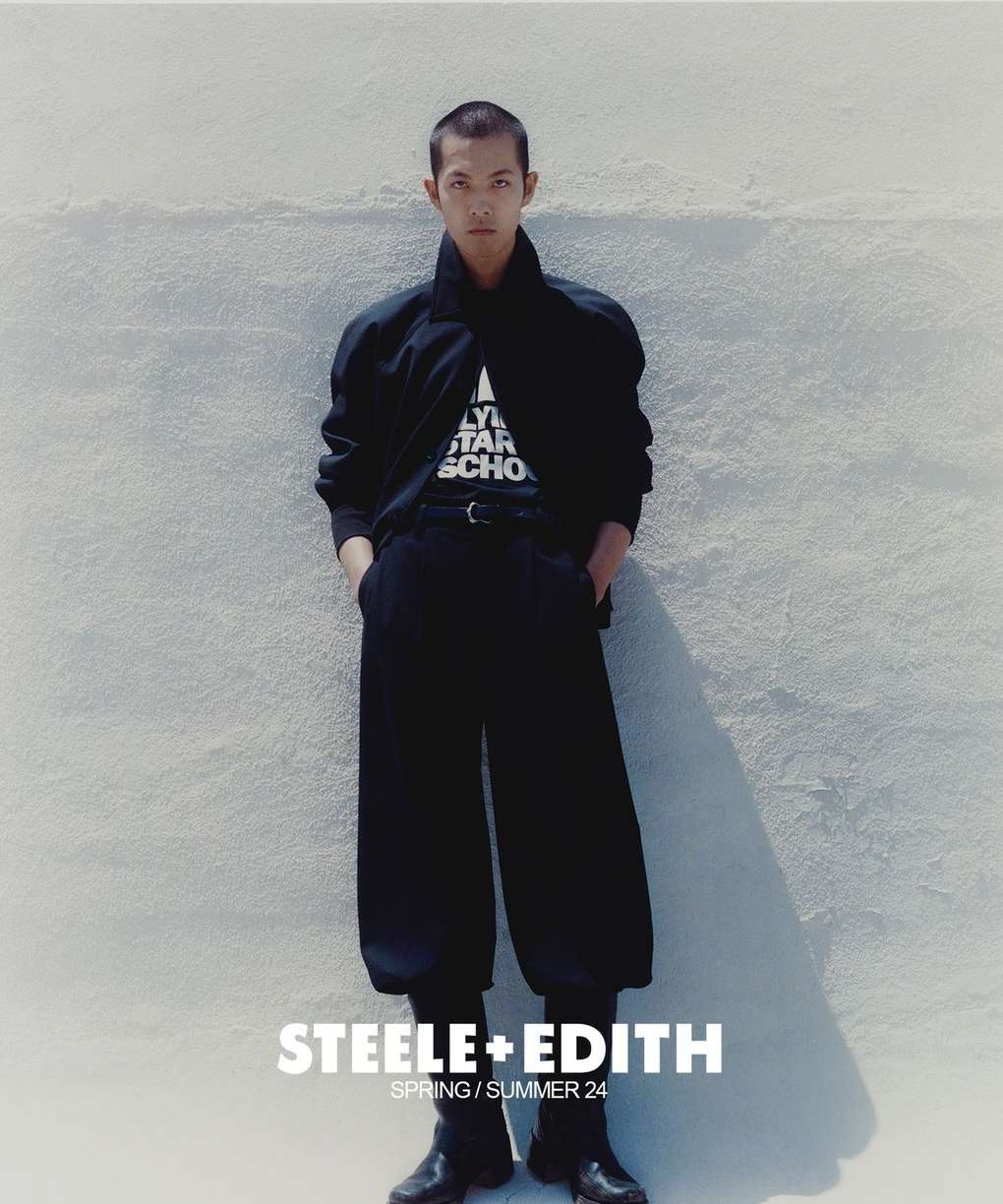 Fashion editorial image of a young adult man in a black outfit posing against a textured wall. The text "STEELE+EDITH" is visible.