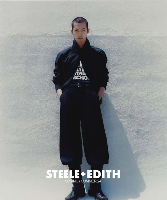 Fashion editorial image of a young adult man in a black outfit posing against a textured wall. The text "STEELE+EDITH" is visible.