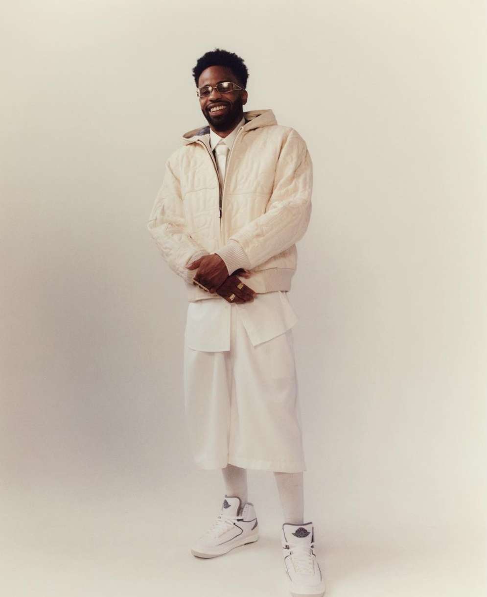 Portrait of a Black man wearing a white puffer jacket and shorts standing against a plain backdrop