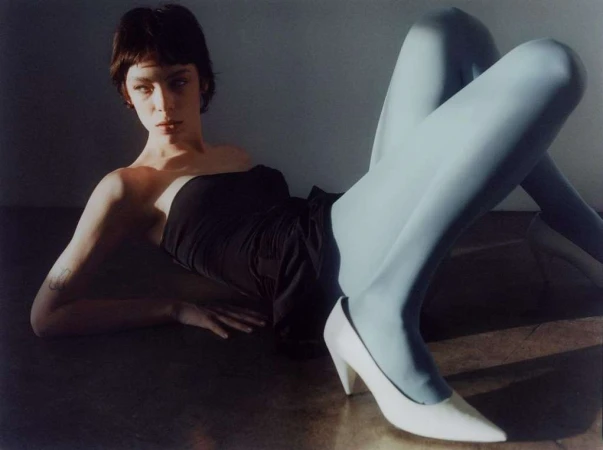 Model in a black strapless top and light blue tights reclining on the floor wearing white high heels