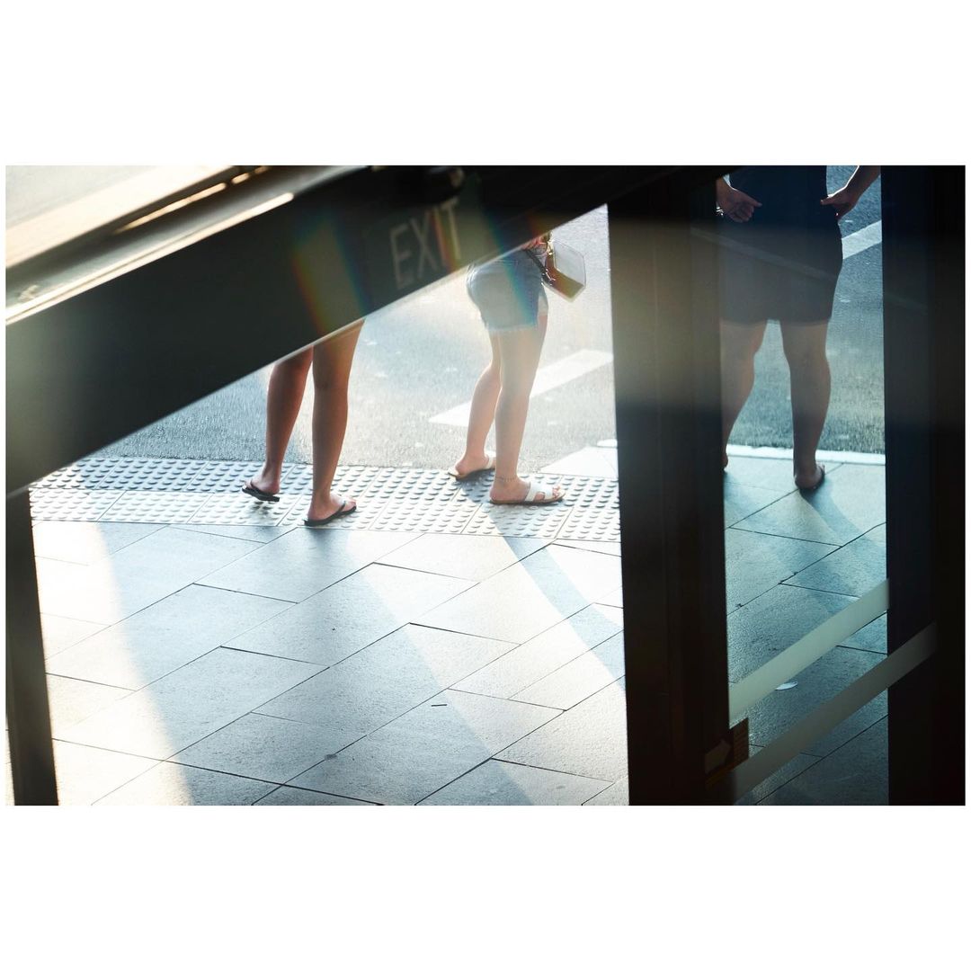 Three women stand near an exit, sunlight shining on the tiled floor. The women wear casual clothing, and the scene is framed by an opening.