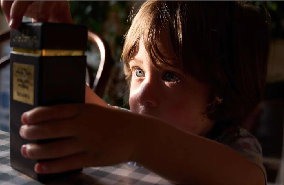 Close-up of a child with blue eyes holding a dark rectangular box with gold accents inside a home environment, looking towards the light.