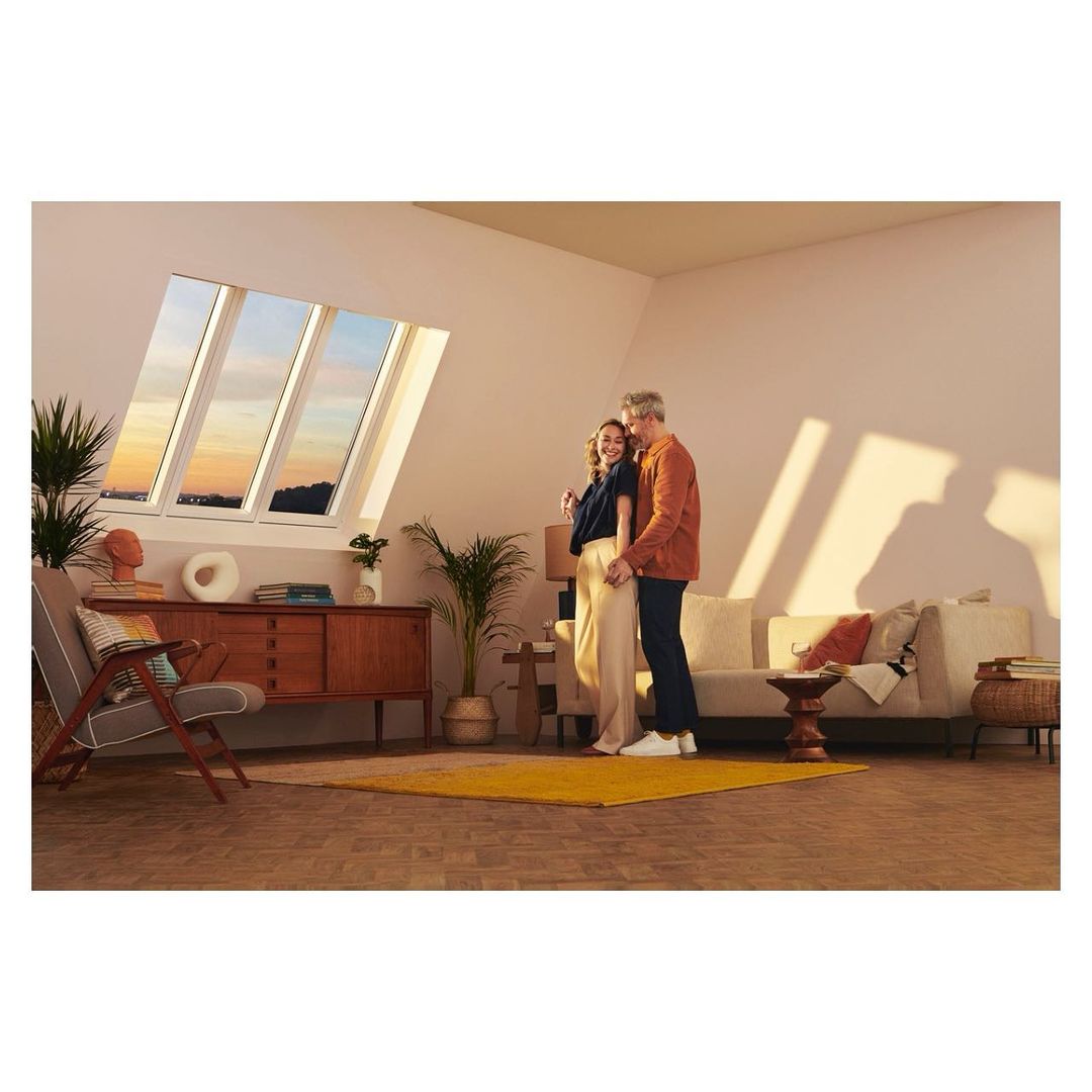 Mature couple embraces in a modern interior with natural light streaming through skylights, complemented by mid-century furniture and decor.