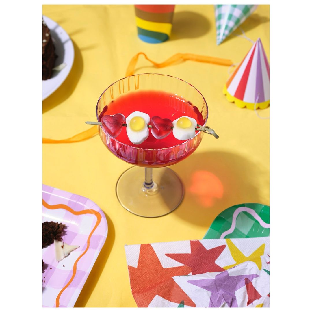 Overhead shot of a party drink with a candy skewer on a yellow tablecloth surrounded by party decorations and partially eaten cake.