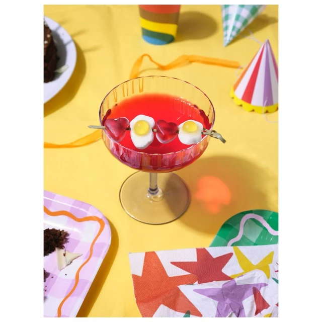 Overhead shot of a party drink with a candy skewer on a yellow tablecloth surrounded by party decorations and partially eaten cake.