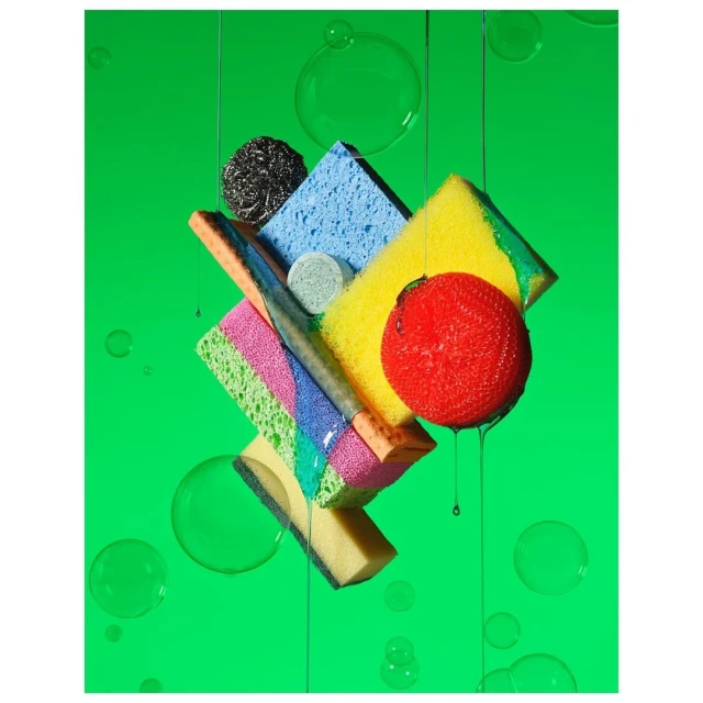 Still life shot of stacked cleaning sponges and steel wool with water droplets against a bright green background. Studio shot, flat lay.