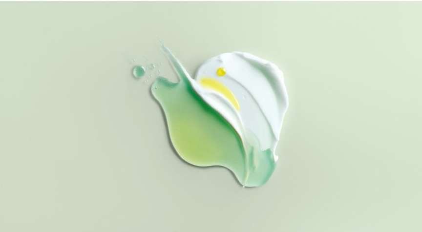 Elevated view of white and green cosmetic cream smears and drops against a solid light-green background in a studio setting.
