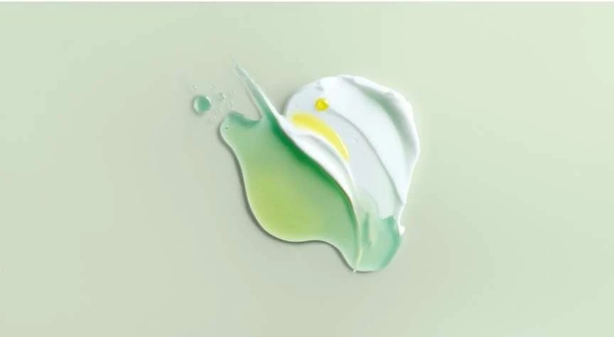 Elevated view of white and green cosmetic cream smears and drops against a solid light-green background in a studio setting.