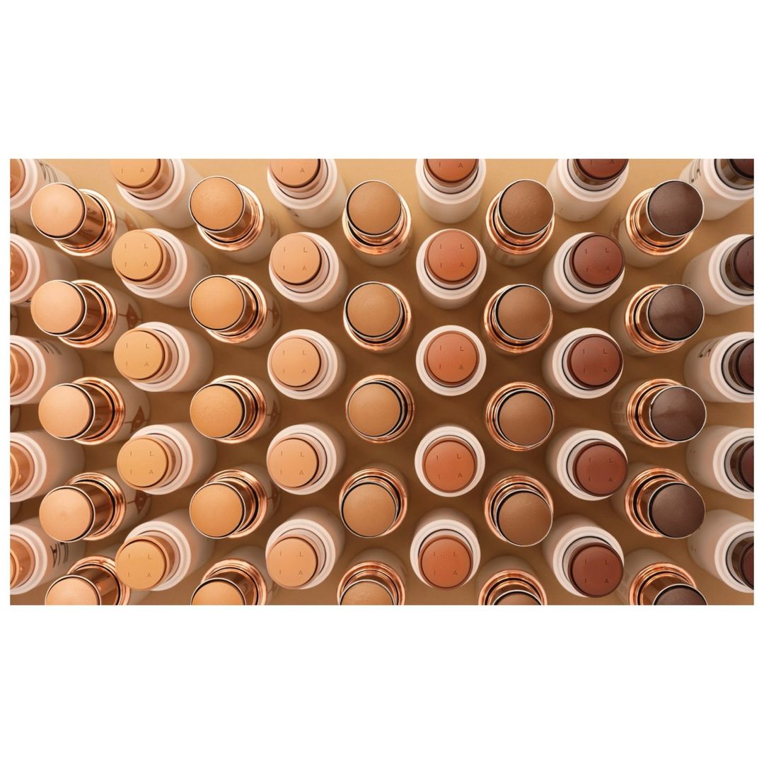 Overhead shot of multiple rows of white and gold cosmetic concealer sticks in varying neutral skin tones, for beauty and makeup concepts.