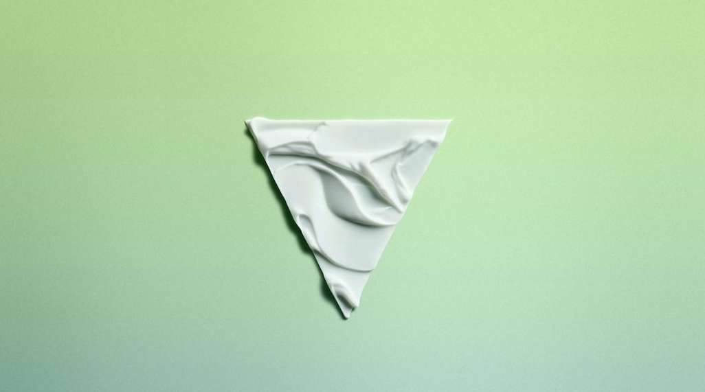 Triangle of white cream substance on a green gradient background. The cream has a rippled texture and fills the triangle shape.