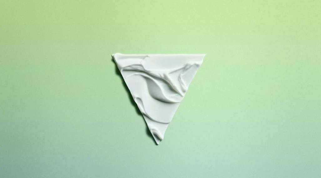 Triangle of white cream substance on a green gradient background. The cream has a rippled texture and fills the triangle shape.