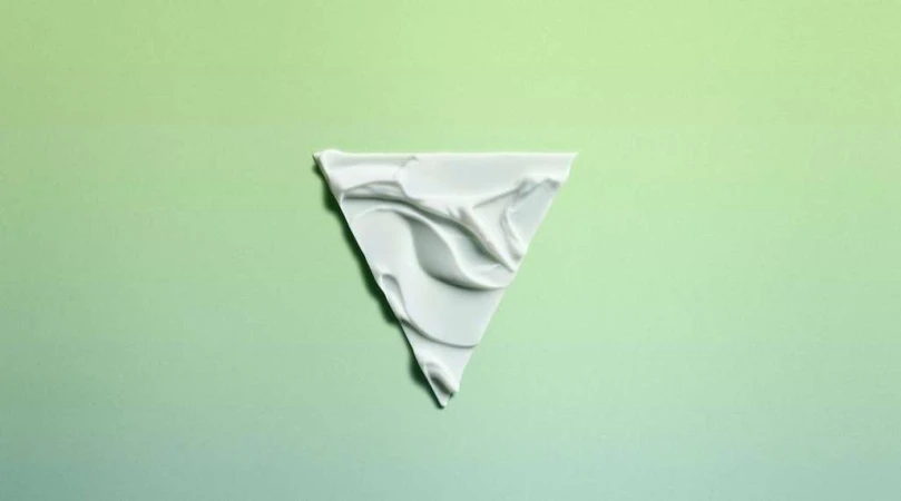 Triangle of white cream substance on a green gradient background. The cream has a rippled texture and fills the triangle shape.