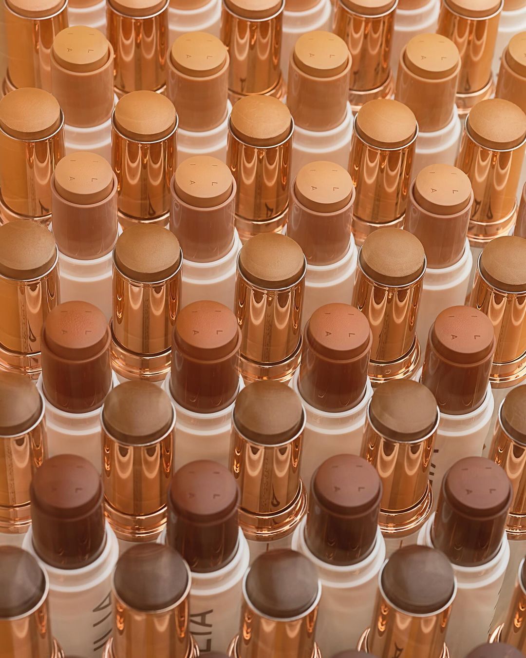 Array of makeup foundation sticks in varying skin tones, closely arranged on a white surface, with a focus on beauty and cosmetics.