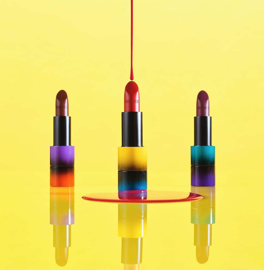 Three lipsticks stand with red liquid dripping on the middle one on a vibrant yellow background creating a striking beauty product shot.