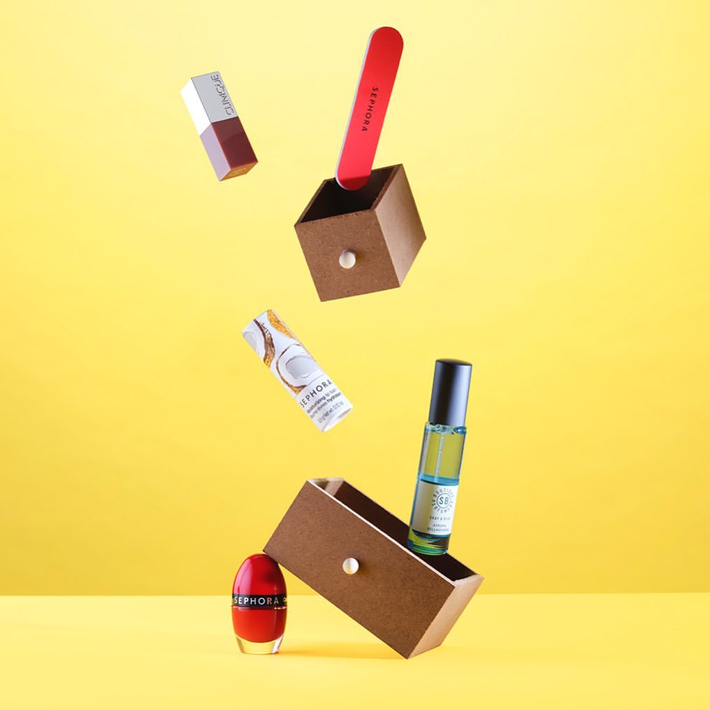 Beauty product still life featuring cosmetic containers and wooden drawers on a vibrant yellow background, arranged in a levitating display.