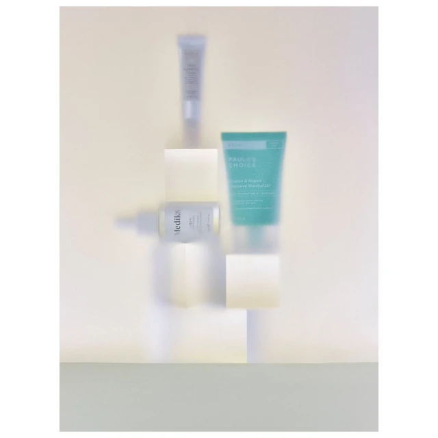 Cosmetic product tubes and bottles arranged on white blocks against a light yellow background in a still life product shot.