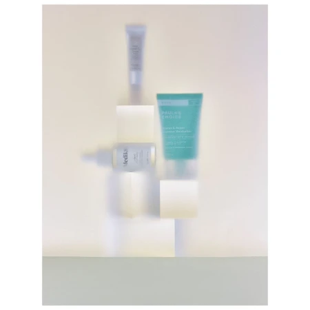 Cosmetic product tubes and bottles arranged on white blocks against a light yellow background in a still life product shot.