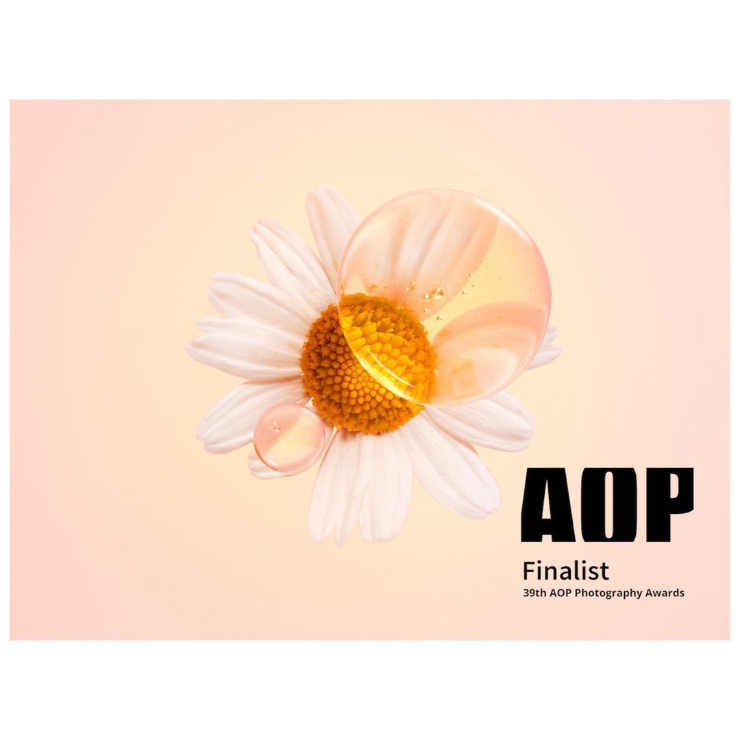 Close-up of a daisy flower with water droplets on a peach background, accompanied by 'AOP Finalist 39th AOP Photography Awards' text.