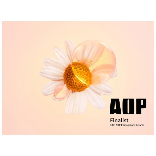 Close-up of a daisy flower with water droplets on a peach background, accompanied by 'AOP Finalist 39th AOP Photography Awards' text.