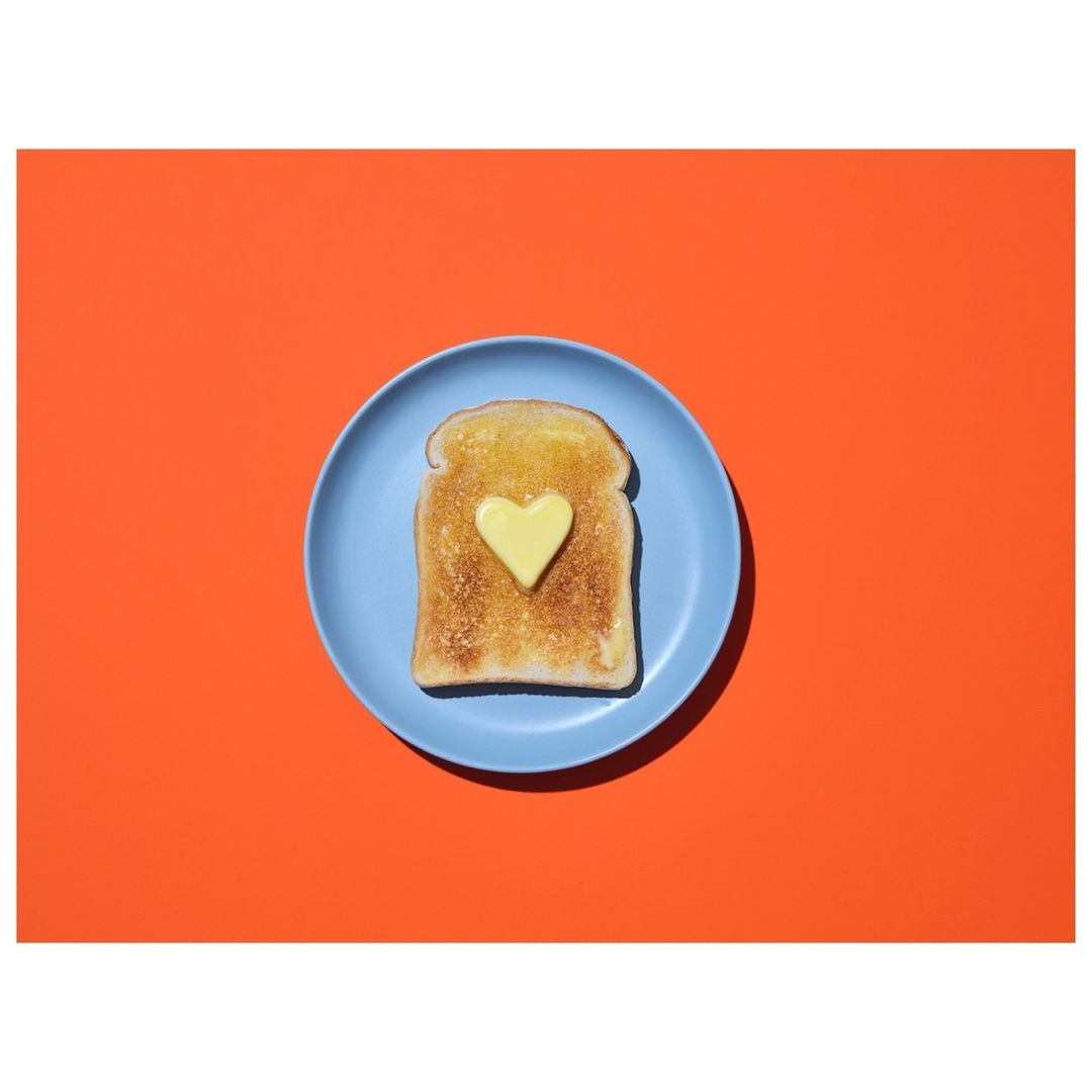 Overhead shot of toast topped with butter cut into a heart shape on a blue plate against a red background. Food photography.