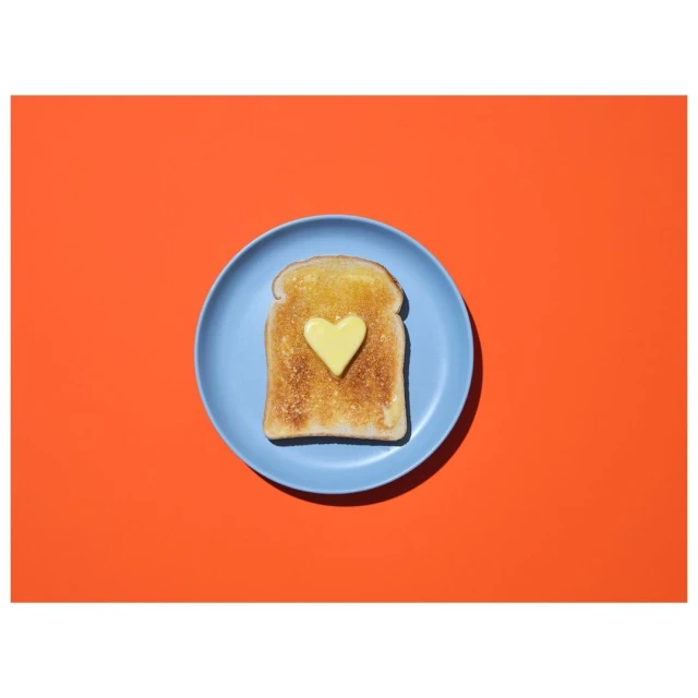 Overhead shot of toast topped with butter cut into a heart shape on a blue plate against a red background. Food photography.