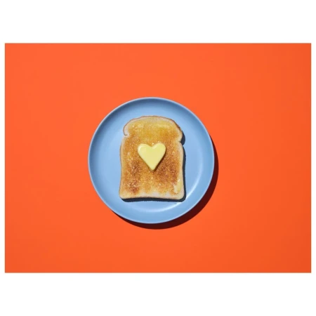 Overhead shot of toast topped with butter cut into a heart shape on a blue plate against a red background. Food photography.