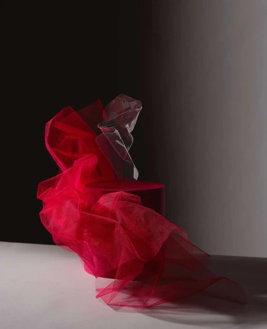 Dramatic studio shot: vibrant pink fabric cascades from a platform, illuminated against a contrasting dark backdrop. Abstract and visually striking.