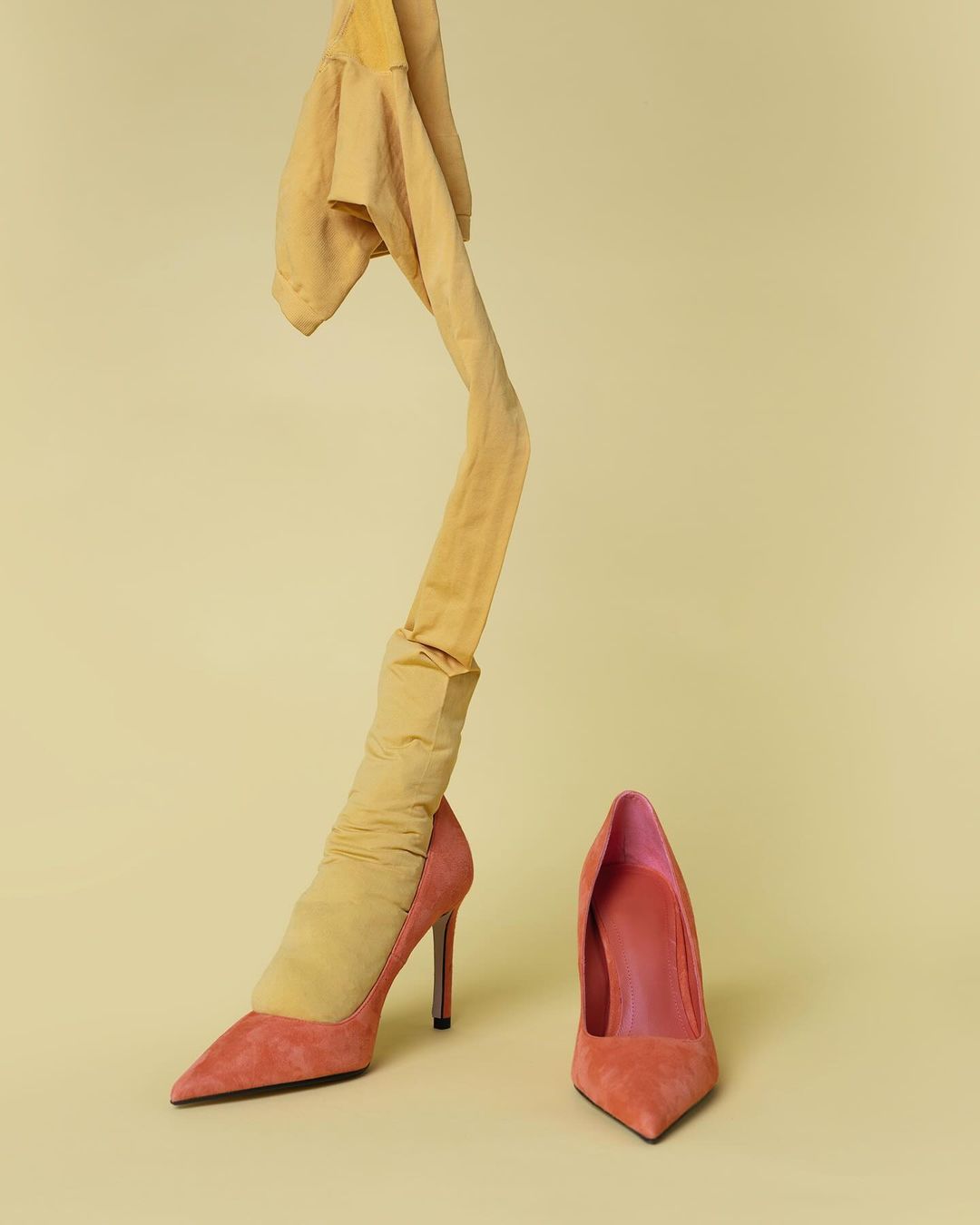 High heel shoes with a hose draped over one, set against a pale yellow background, creating a striking fashion still life.