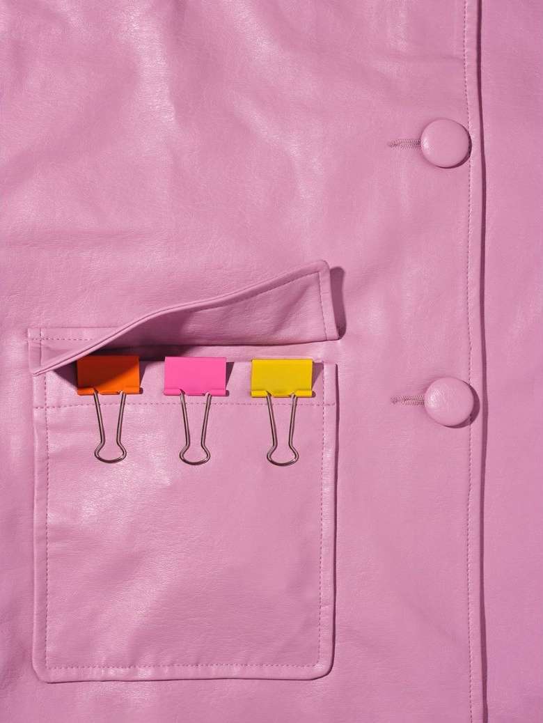Close-up shot of a pink leather jacket with a pocket holding colorful binder clips, lit with studio lighting.