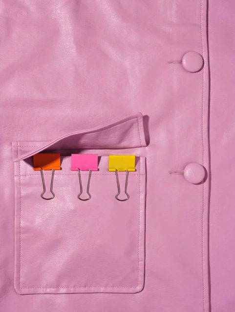 Close-up shot of a pink leather jacket with a pocket holding colorful binder clips, lit with studio lighting.