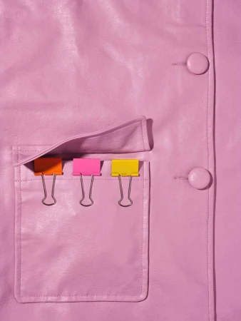 Close-up shot of a pink leather jacket with a pocket holding colorful binder clips, lit with studio lighting.