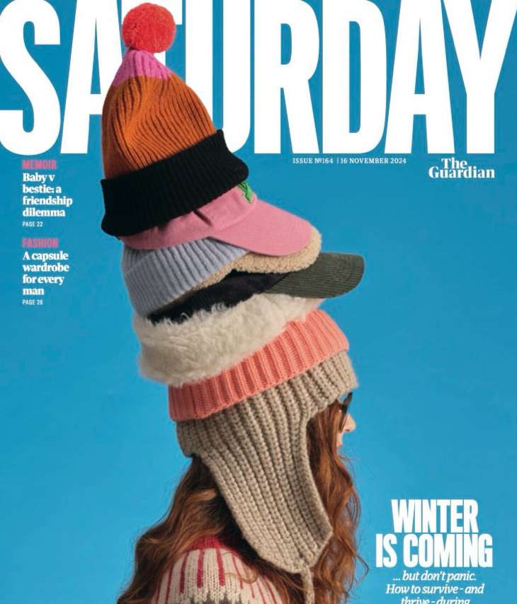 Magazine cover featuring a woman with red hair wearing multiple knit hats stacked on her head against a vibrant blue background.