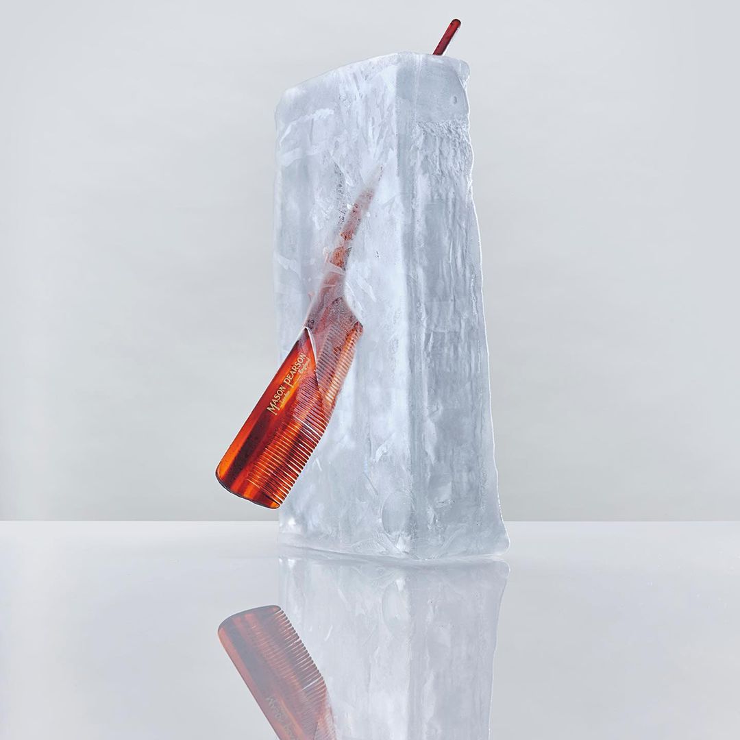 Still life shot of a brown comb frozen in a clear block of ice with red straw. The setting is simple with white background.