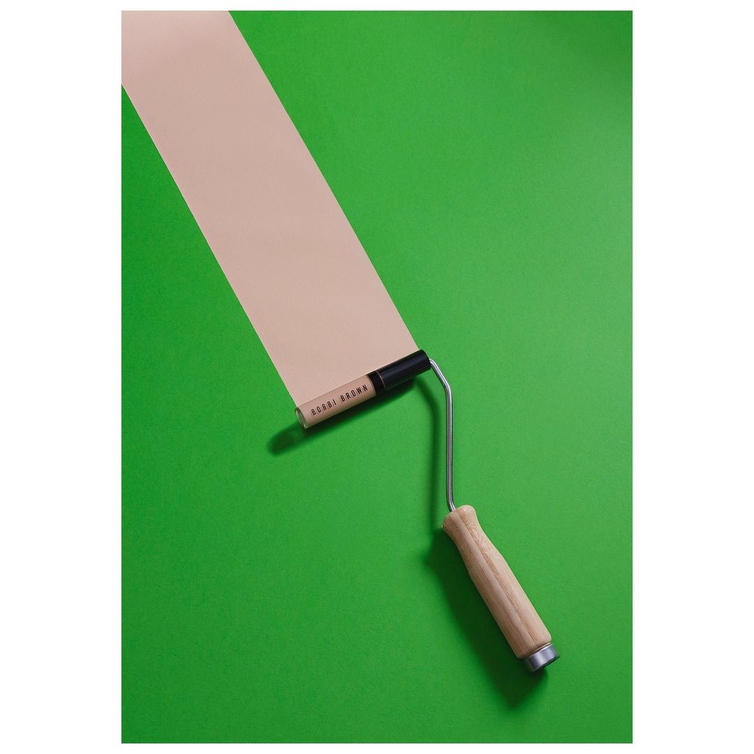 Close-up studio shot of a paint roller with light brown paint rolled onto a vibrant green background, creating a graphic and modern aesthetic.