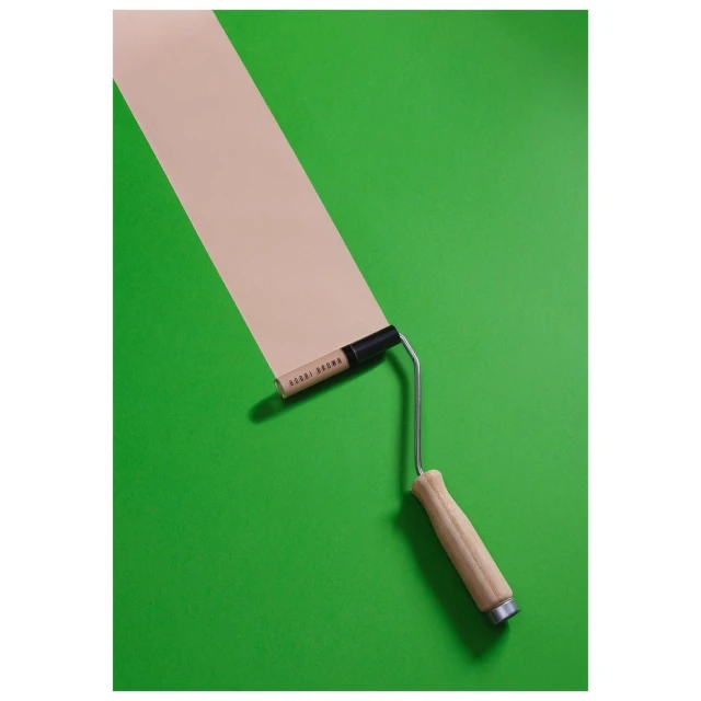 Close-up studio shot of a paint roller with light brown paint rolled onto a vibrant green background, creating a graphic and modern aesthetic.