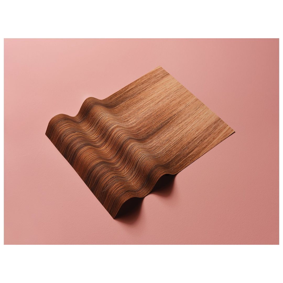 Wavy brown and caramel hair swatch displayed on a pink background. Texture and colour for hairdressing and beauty concepts.