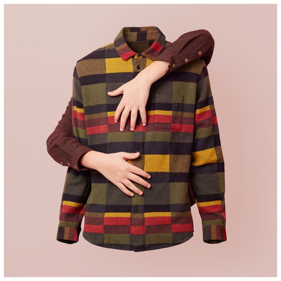 Checkered flannel shirt with hands in an indoor setting. Stylish and versatile clothing design with warm hues, soft textures.