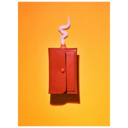 Orange leather wallet with pink cream squirting out against a solid yellow backdrop, photographed by Kellie French
