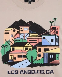 Close-up of a beige crewneck t-shirt featuring a colorful graphic illustration of city buildings and mountains by Kelly Malka.