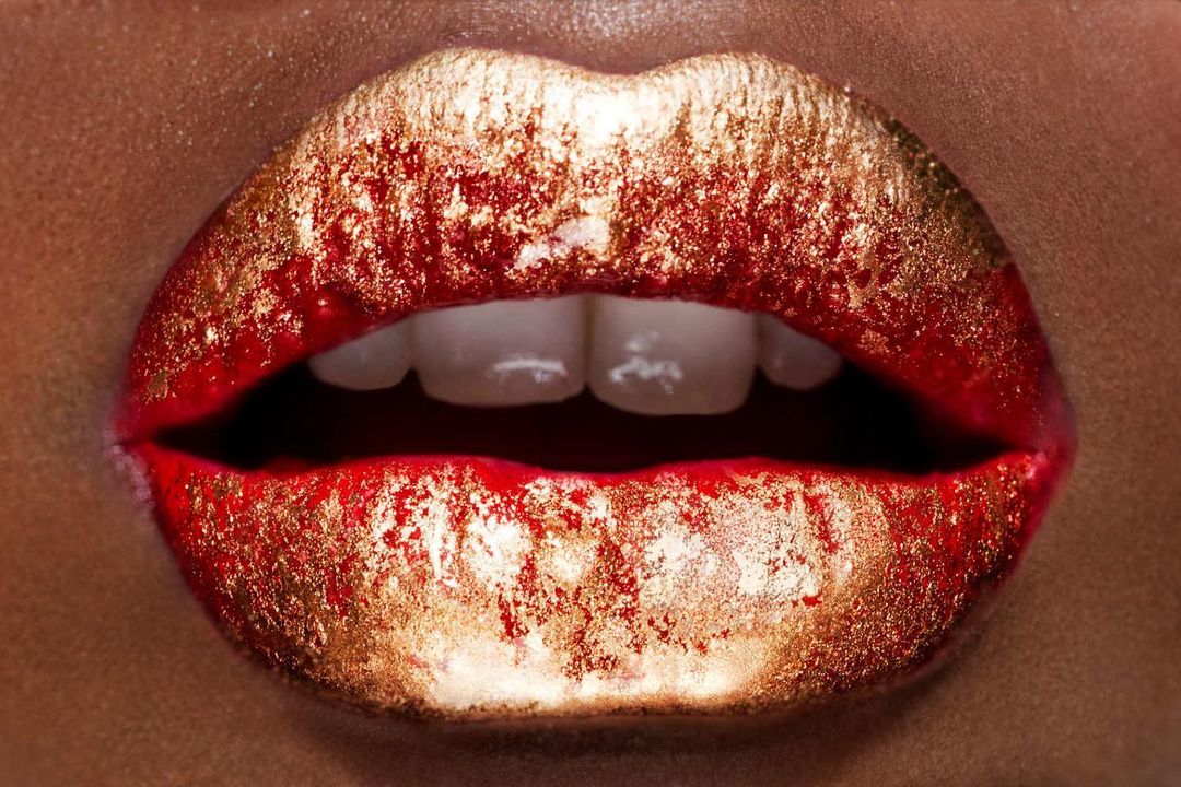 Close-up of adult female's mouth with red and gold glitter lipstick displaying teeth, beauty fashion close-up, beauty product photography.