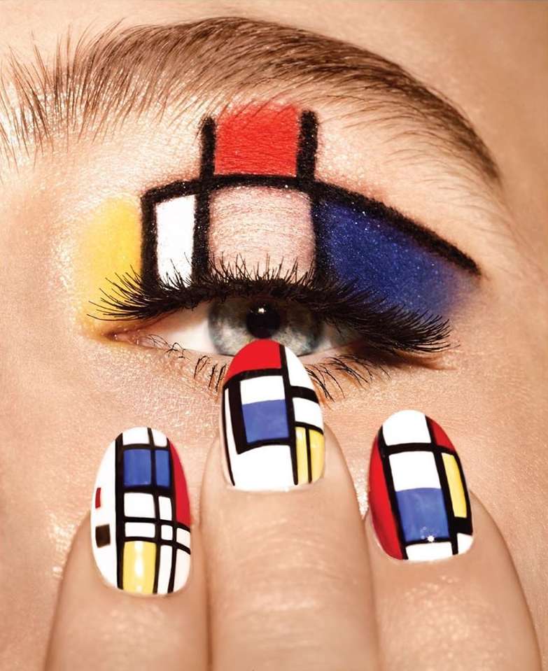 Close-up of a woman's eye with Mondrian-inspired eye makeup and matching nail art featuring red, blue, yellow, black, and white blocks.