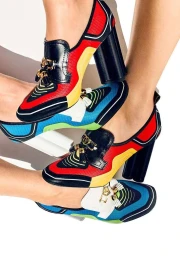 Close-up of legs wearing colourful high-heeled loafers with gold horsebit hardware against white background